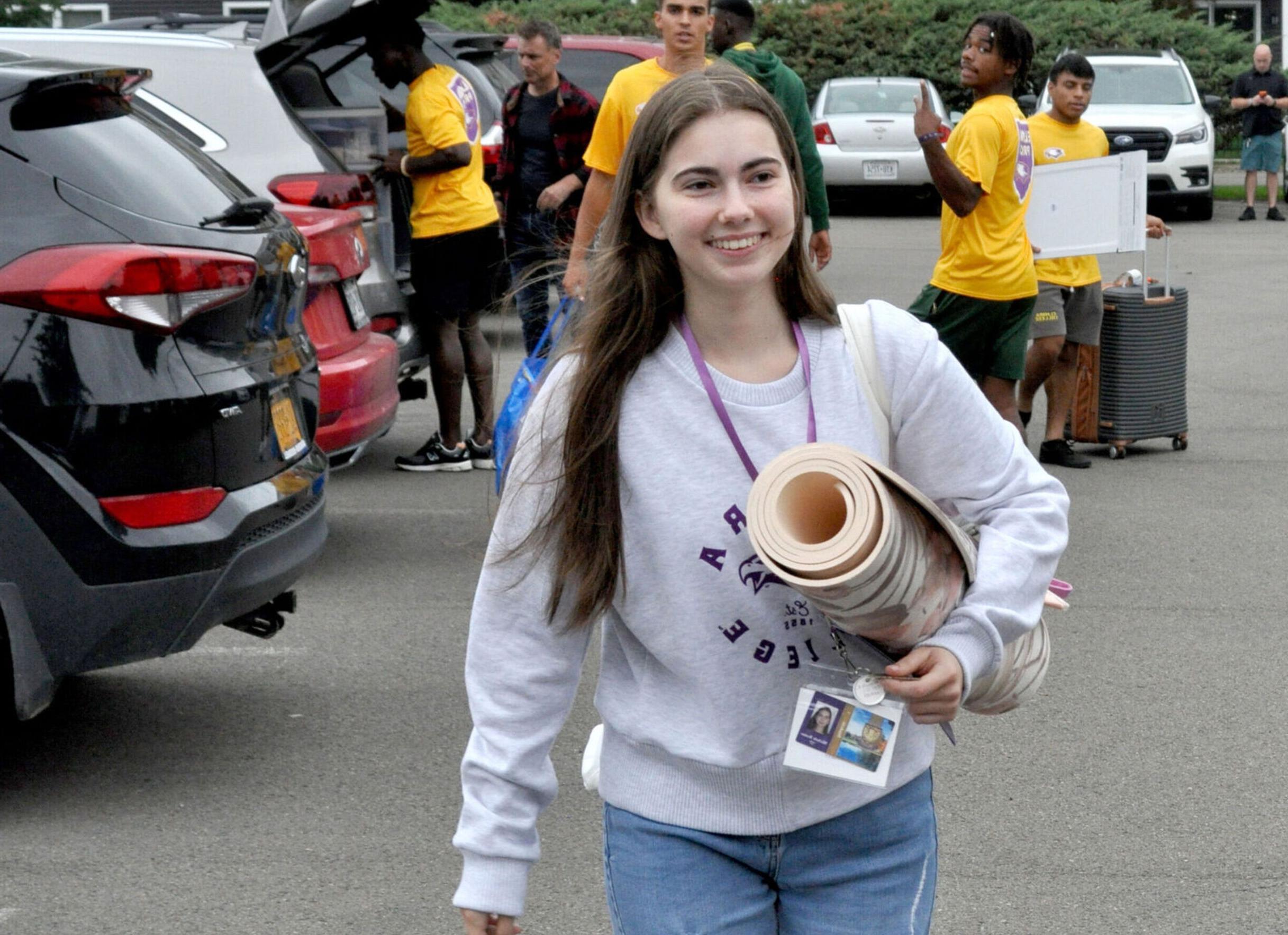 A new female student carries a rug across the parking lot during move-in day